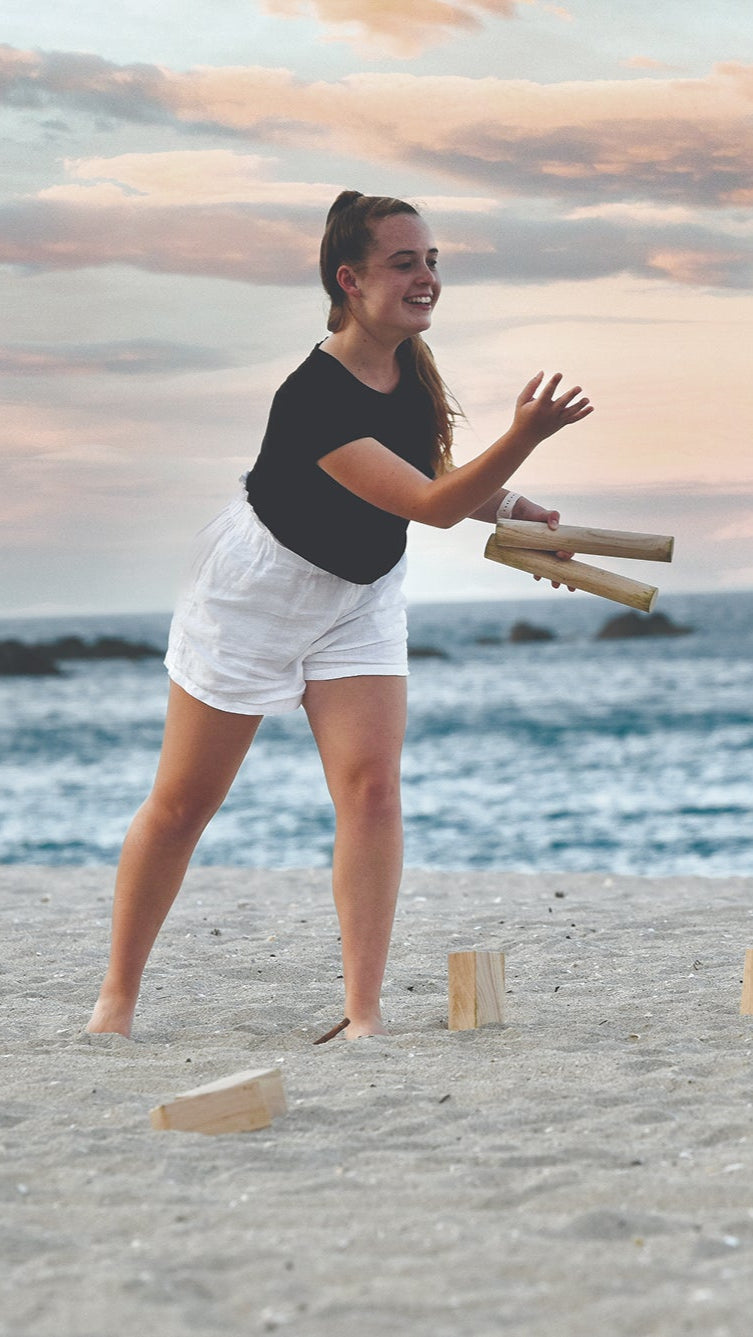 Woman playing Kubb on a beach at sunset