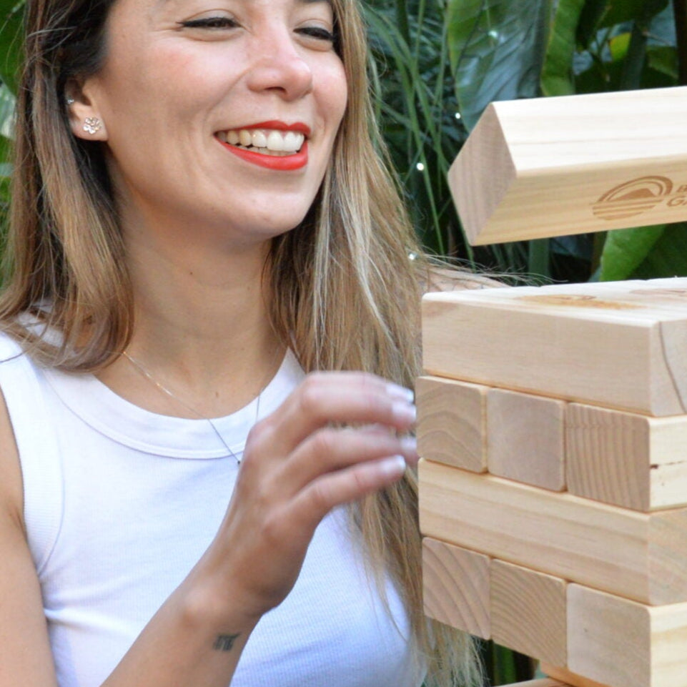 Two women playing with a wooden block tumbling tower game outdoors.