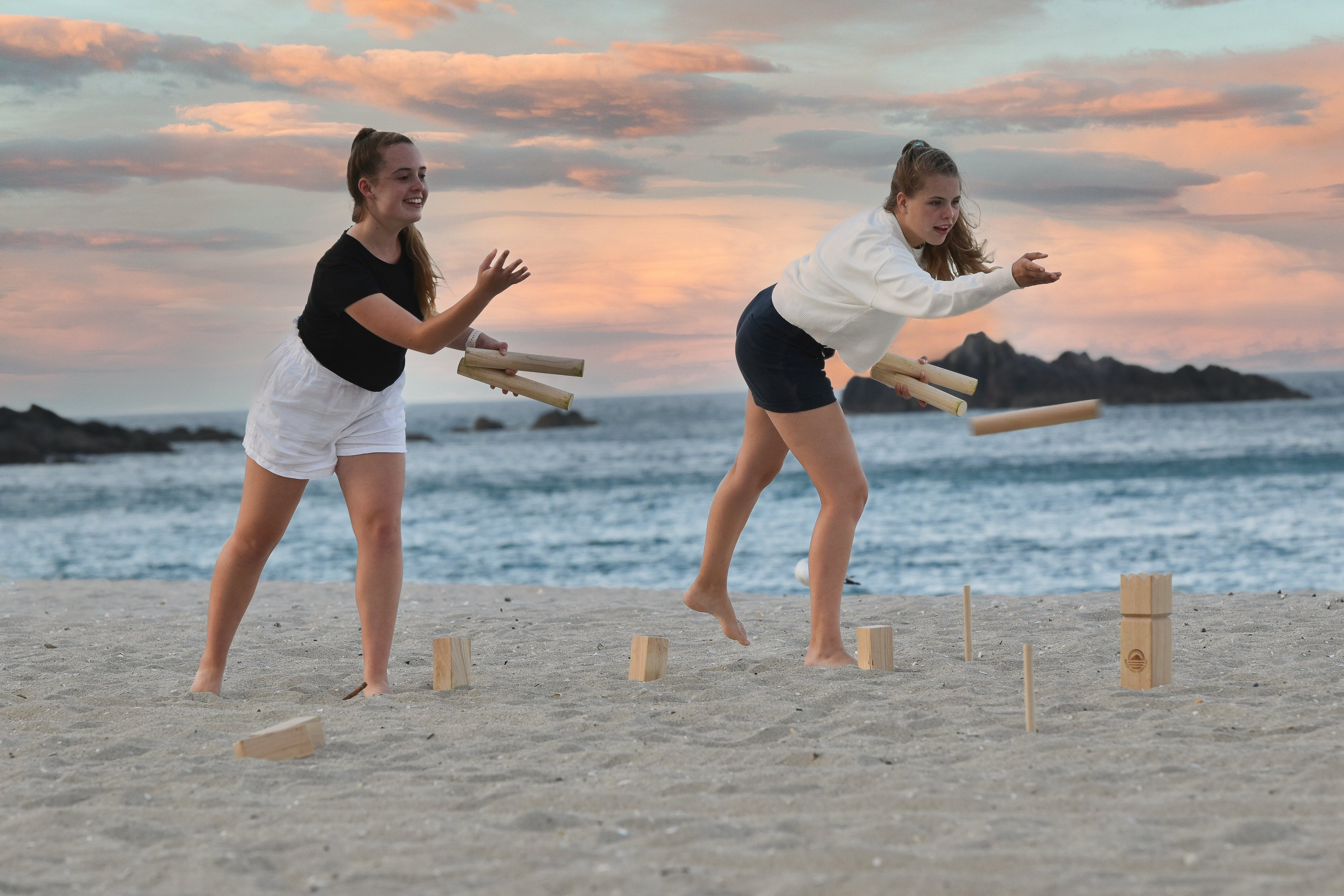 Two girls throwing Kubb sticks on the beach