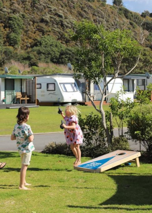 Family playing cornhole in a grassy area with caravans in the background