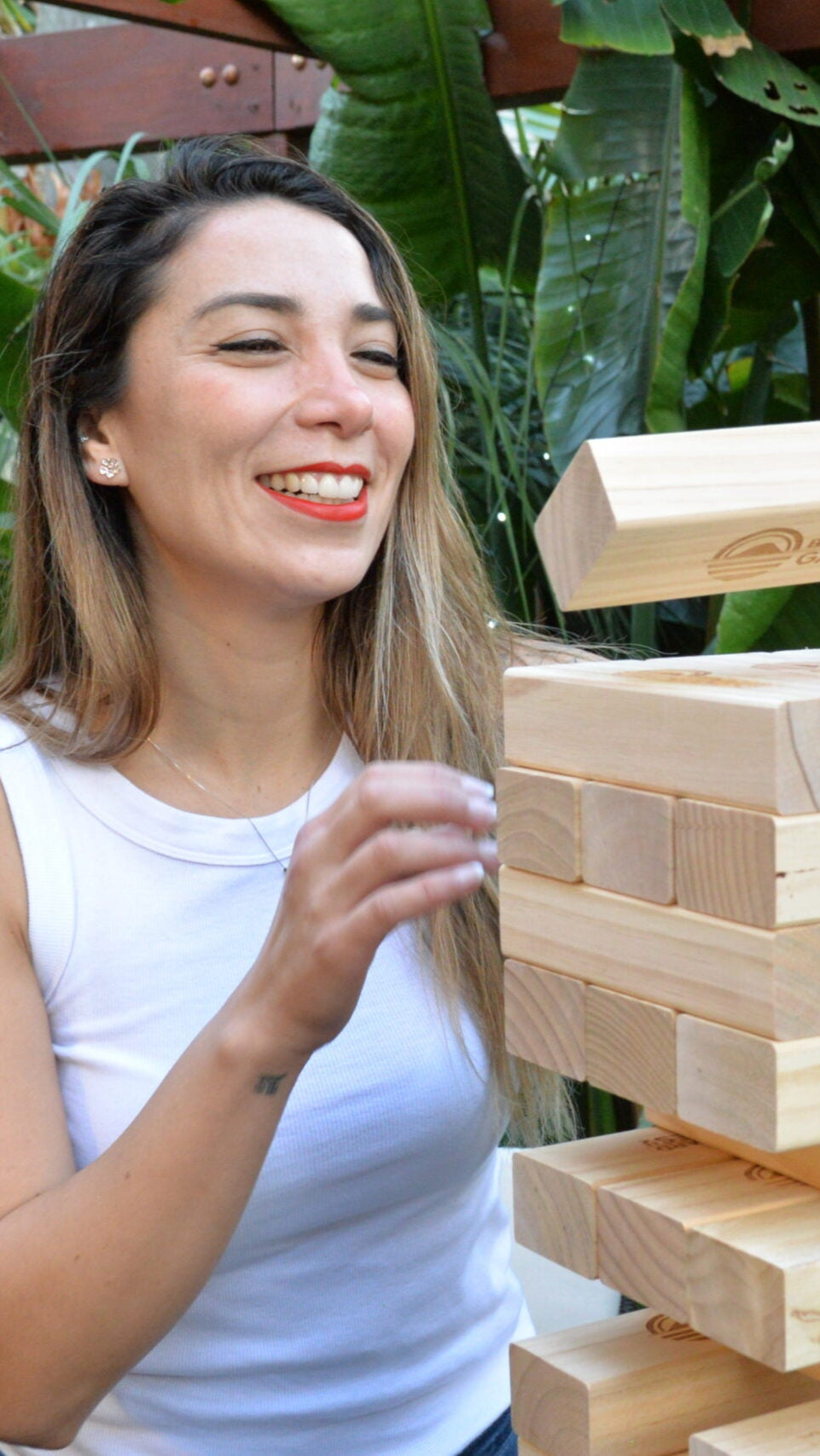 Two women playing with a wooden block tumbling tower game outdoors.