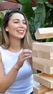 Two women playing with a wooden block tumbling tower game outdoors.