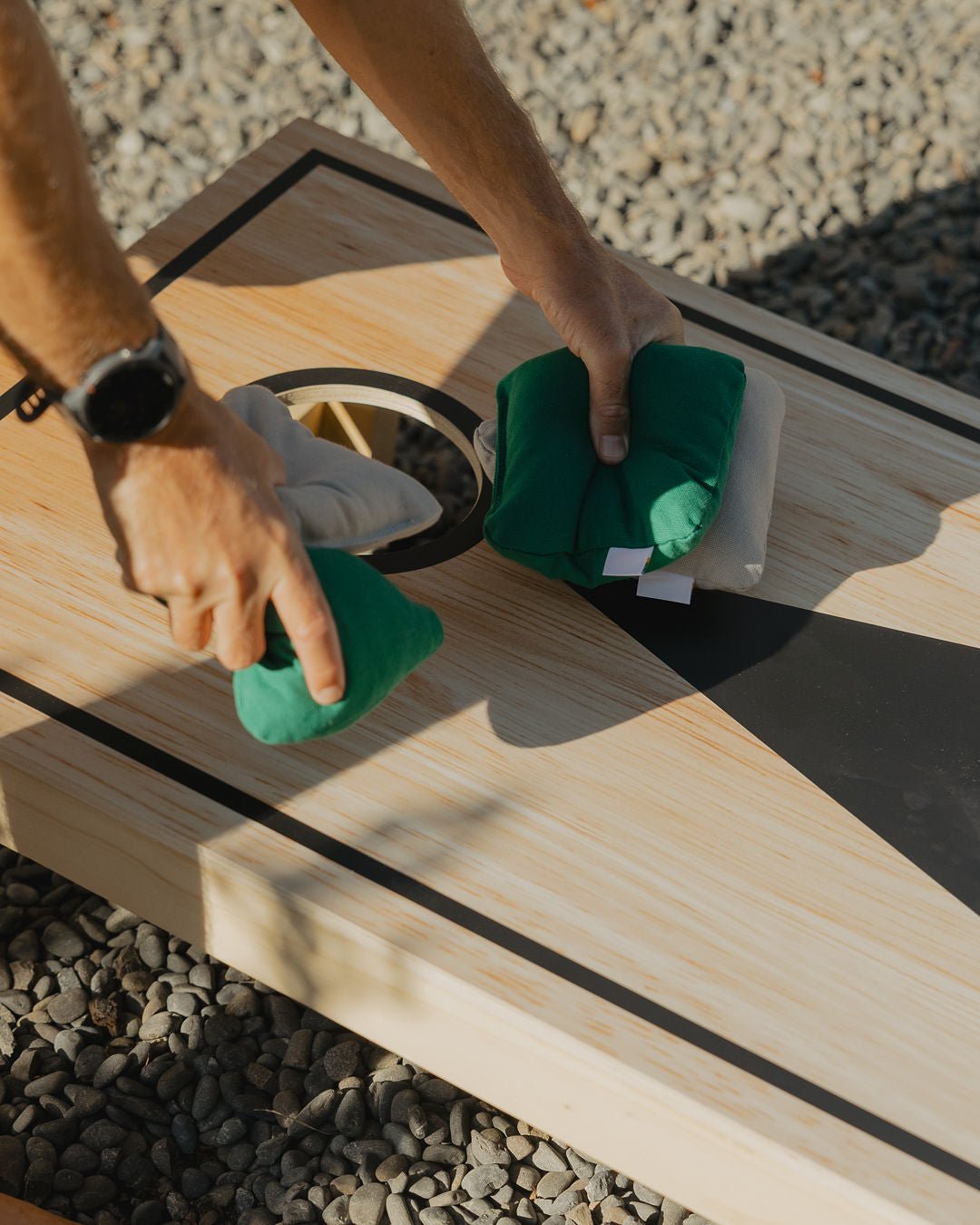 Man picking up grey and green cornhole throwing bags off a Cornhole 
