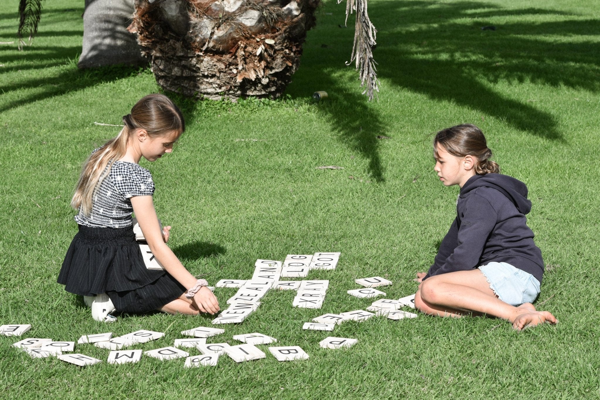 Two Girls Playing Backyard Games Giant Letter Tiles on the lawn