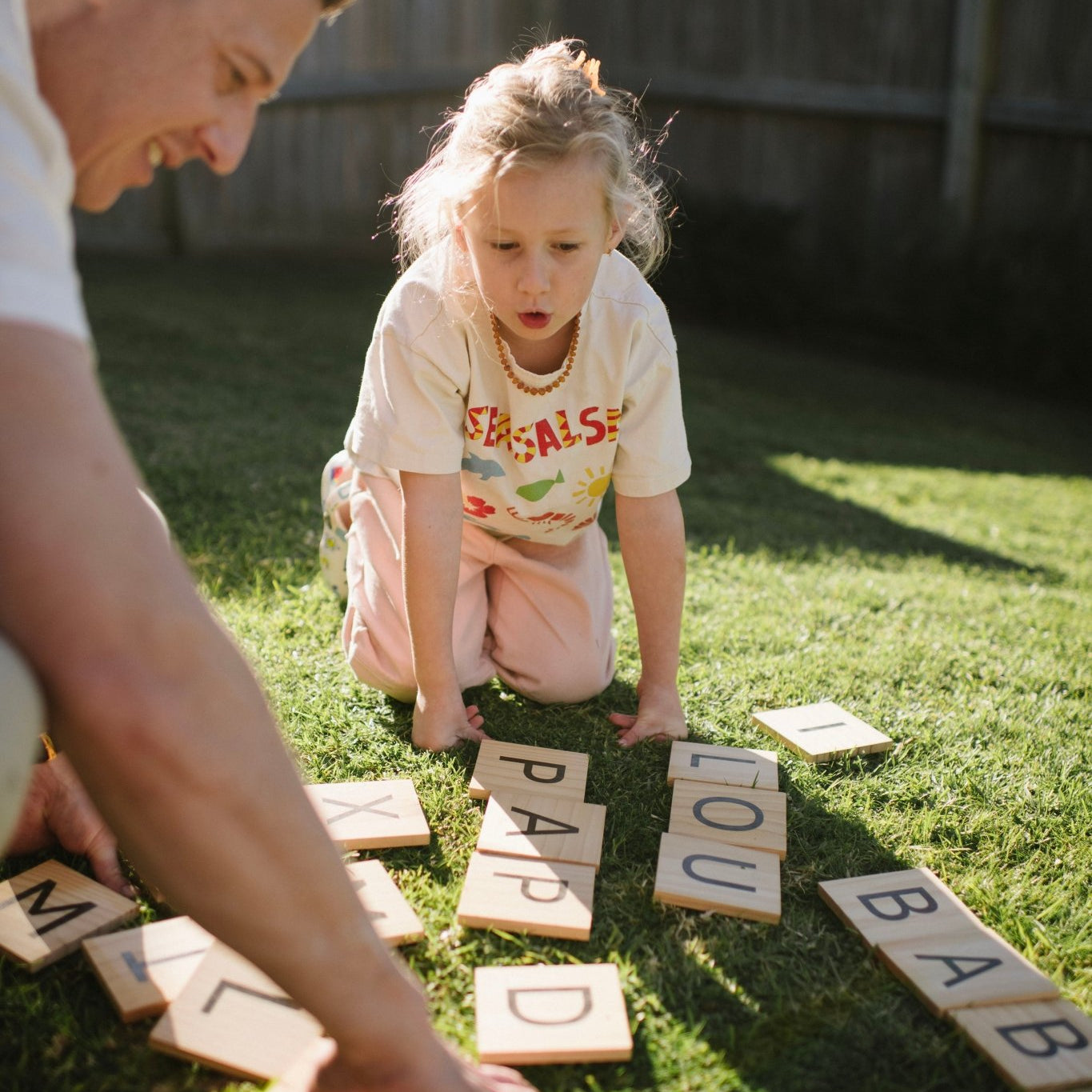 Man and young girl playing with Backyard Games NZ letter tiles on grass