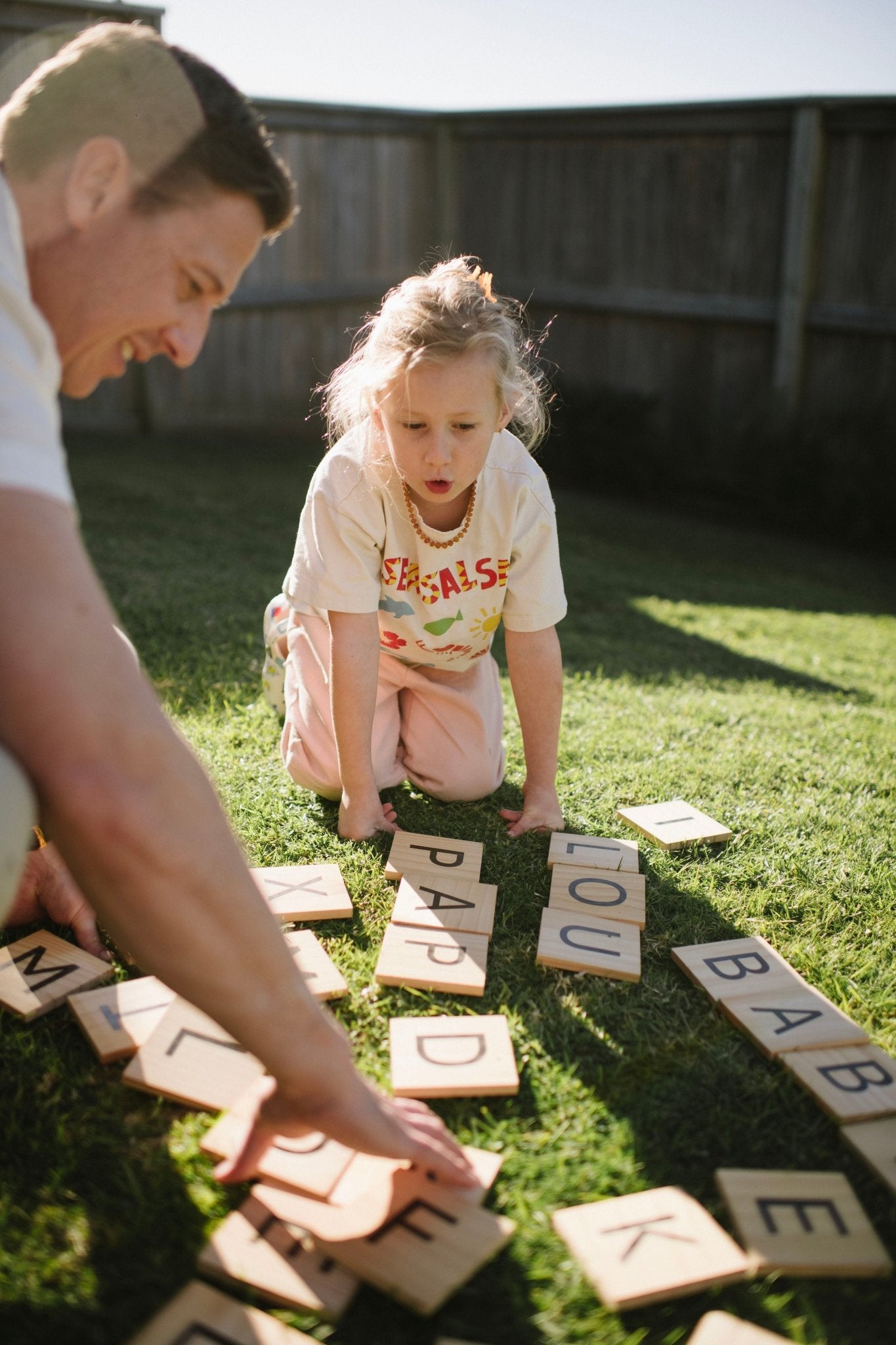 Man and young girl playing with Backyard Games NZ letter tiles on grass