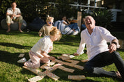Two adults and two children playing Backyard Games Giant Dominoes on a grassy outdoor area.