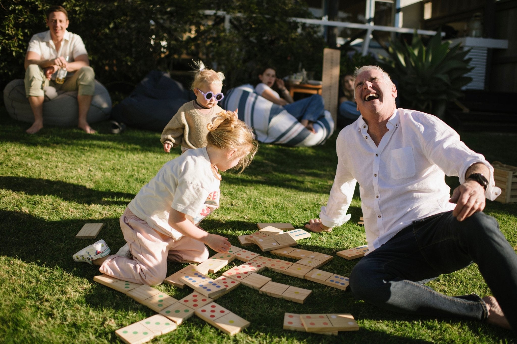 Two adults and two children playing Backyard Games Giant Dominoes on a grassy outdoor area.