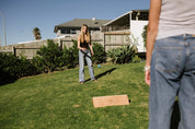 Two people playing a game of Backyard Games NZ Gutterboard on a grassy lawn with a house in the background.