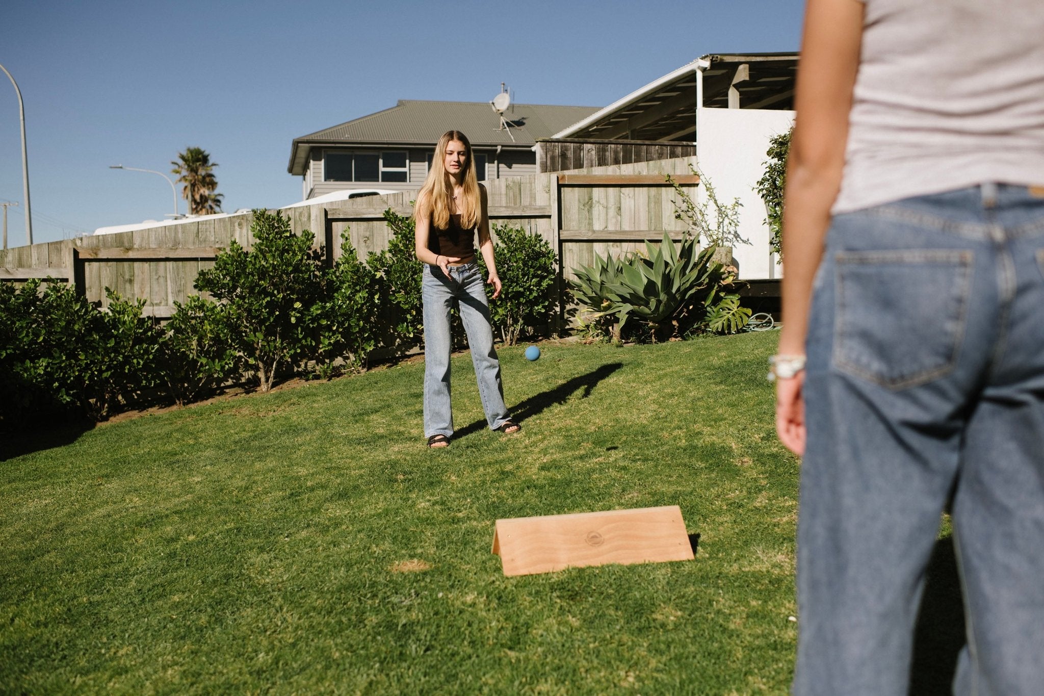 Two people playing a game of Backyard Games NZ Gutterboard on a grassy lawn with a house in the background.