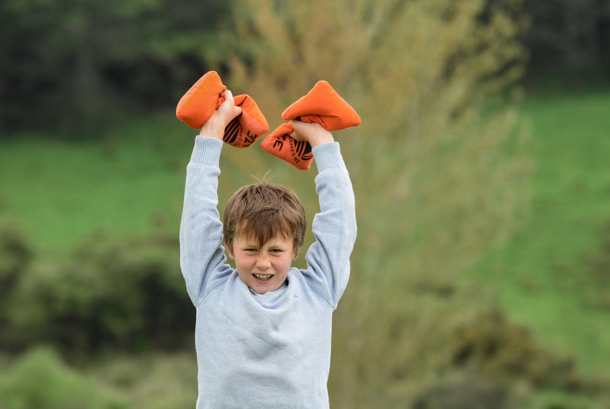 Child holding Backyard Games Pro Cornhole bags in celebration with blurred natural background