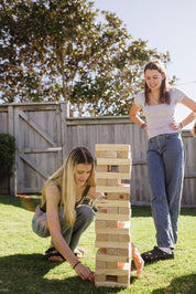 Two women playing with a Backyard Games NZ Super Giant Tumbling Tower outdoors.