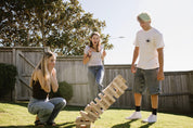 Three people playing Super Giant Tumbling Tower in a backyard.