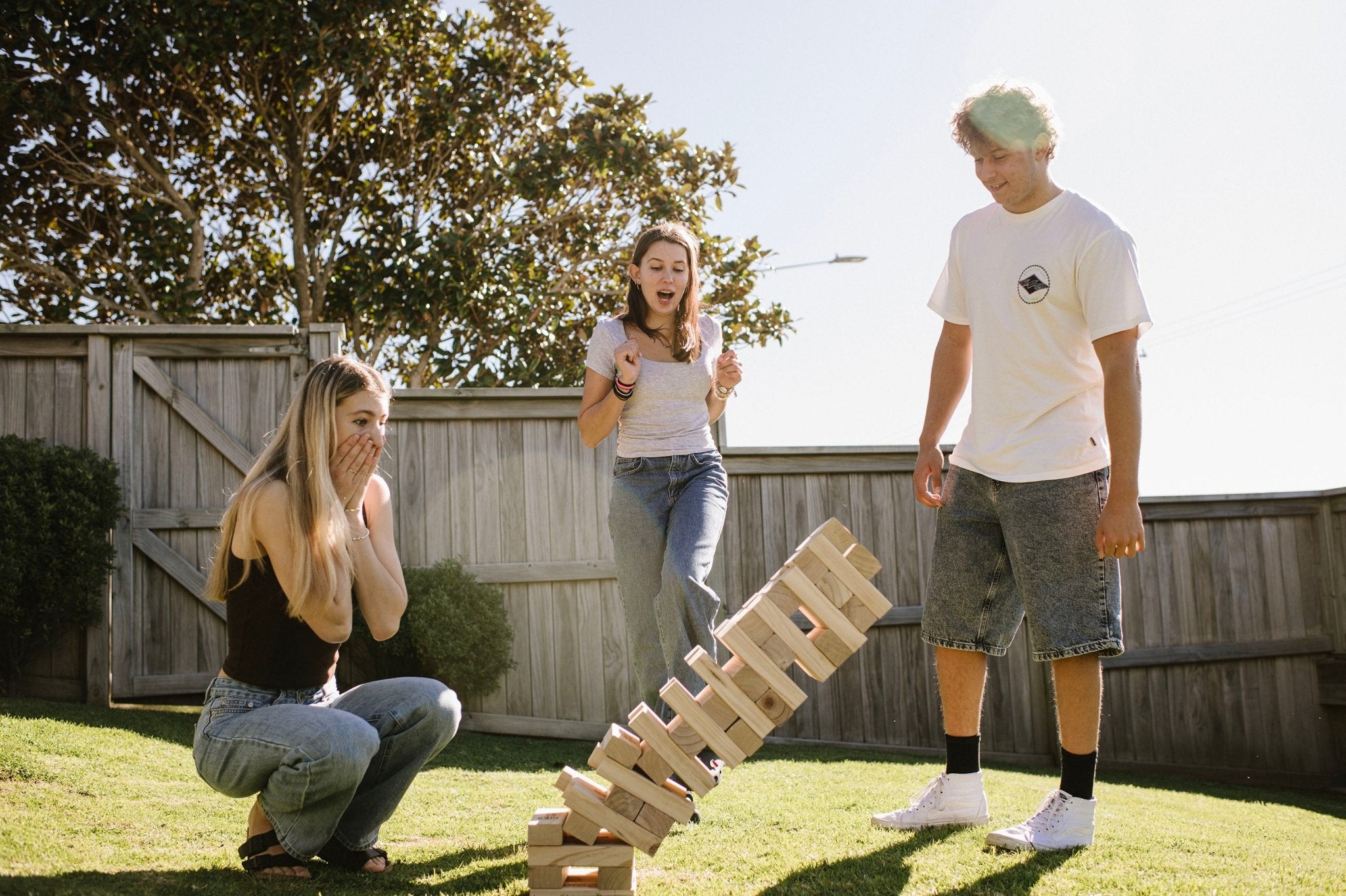 Three people playing Super Giant Tumbling Tower in a backyard.